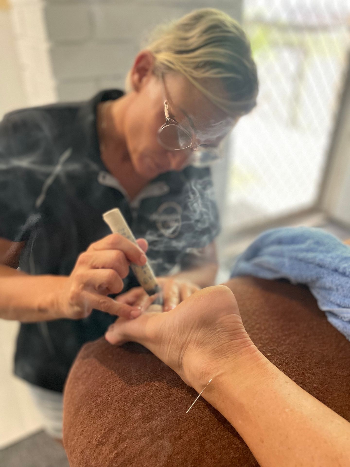 A practitioner holding a lit moxibustion stick over a foot, acupuncture mugwort, 